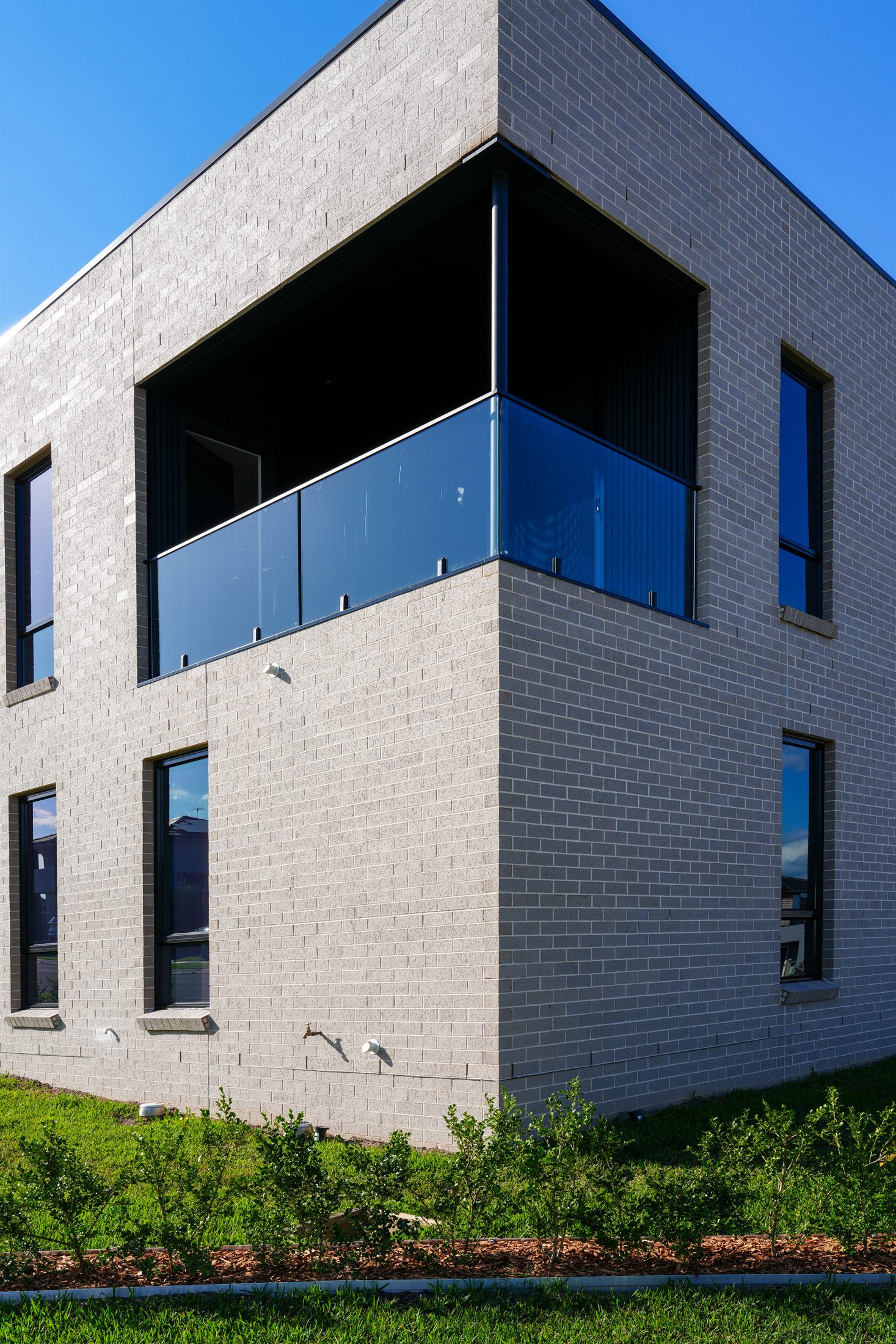 A finished custom two-storey brick home with a glass balustrade balcony, built by Auzzy Projects in Western Sydney